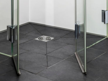 square shower drain on dark tile floor inside glass shower, bathroom maintenance context