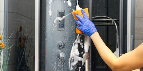 Hand cleaning glass shower screen with sponge and soap suds