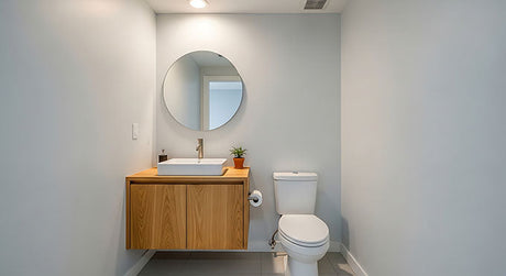 Modern compact powder room with a floating wooden vanity, white vessel basin, and round mirror
