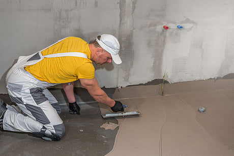 contractor leveling bathroom floor with trowel during renovation preparation near unfinished wall