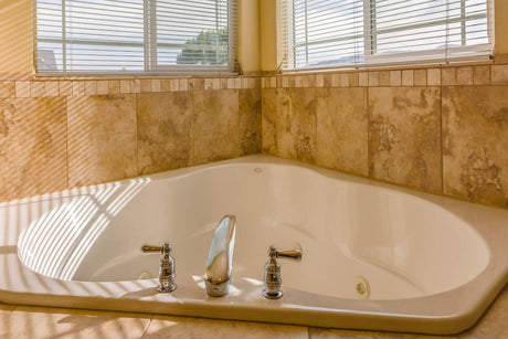 Corner spa bath with built-in jets and tiled surround in home bathroom.