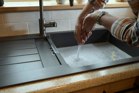 Using drain snake tool to clear clogged kitchen sink with standing water.