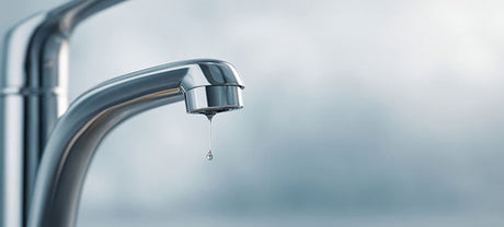 Chrome tap with a single water droplet falling against a soft blue background
