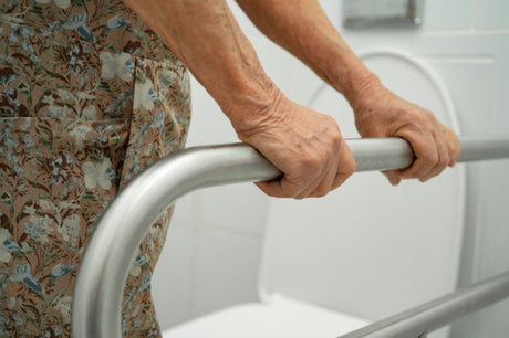 Elderly person gripping bathroom grab bar for support near toilet in accessible bathroom.