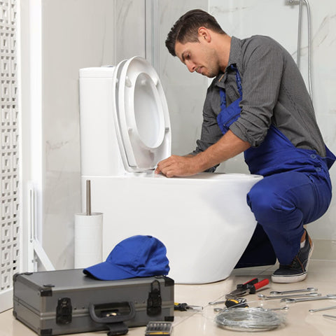 Plumber is fixing a toilet, surrounded by tools and equipment in a bathroom setting.