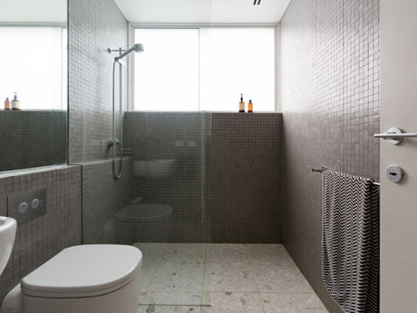 Frameless glass walk-in shower with gray tile walls, rainfall showerhead, and frosted window.