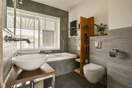 gray tile bathroom with vessel sink, bathtub, wall-mounted toilet, and large window