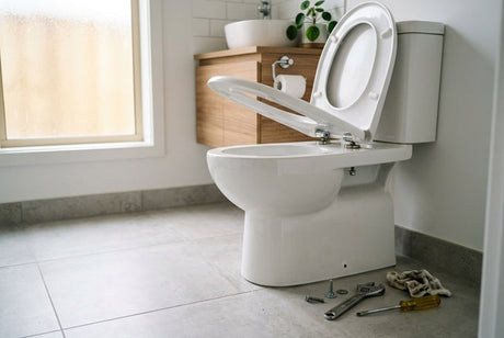 White toilet with open seat and plumbing tools on grey tiled floor