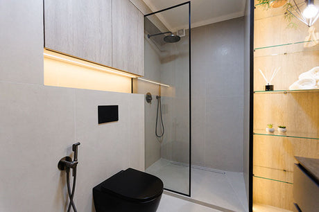Modern bathroom with black wall-hung toilet, bidet tap, and glass walk-in shower