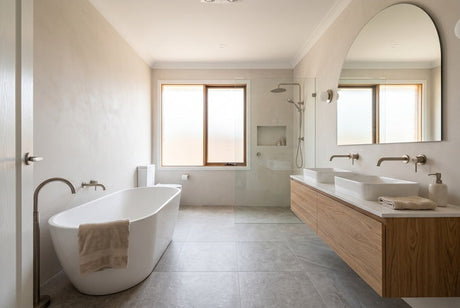 Renovated bathroom with white freestanding bath, timber vanity, double basins and arched mirror