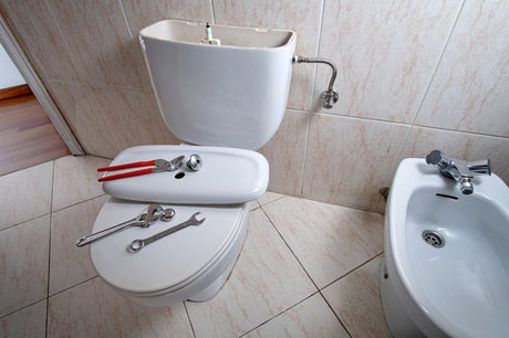 Toilet cistern repair tools on bathroom toilet beside bidet and tiled wall