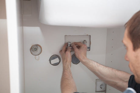 Plumber's hands connecting chrome mixer tap fittings inside a wall cavity
