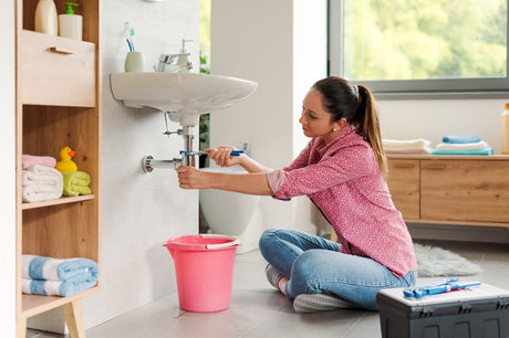 Woman in pink shirt using wrench on bathroom sink tap pipes
