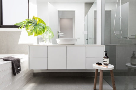 Floating white bathroom vanity with vessel basin, monstera plant, and timber stool