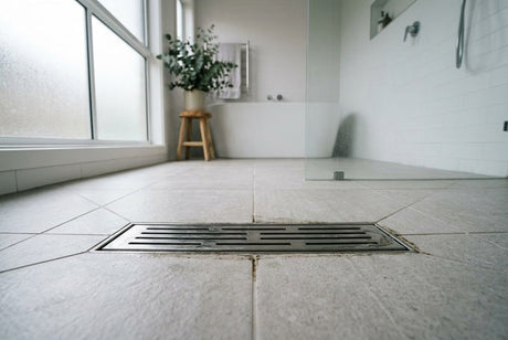Close-up of stainless steel linear shower drain on grey tiled bathroom floor