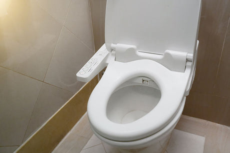 White bidet toilet seat with side control panel in beige tiled bathroom