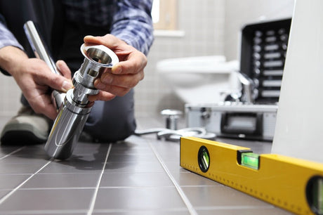 Plumber assembling chrome toilet fitting beside spirit level and tool case