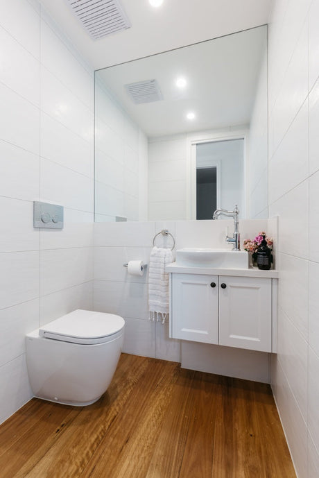 Wall-hung white toilet beside floating vanity with timber floorboards and large mirror