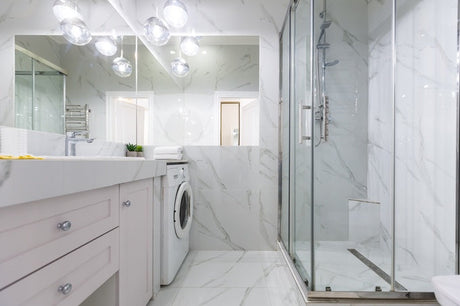Modern bathroom with white marble tiles, glass shower, vanity and washing machine