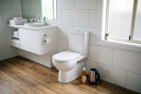 White toilet beside floating vanity, dish soap and kettle on timber floor