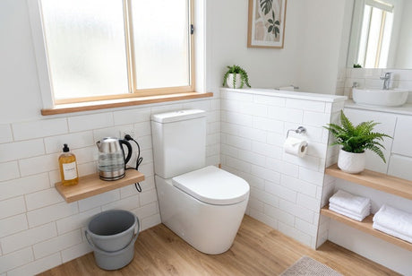 Bright white bathroom with toilet, subway tiles, timber shelves and grey bucket