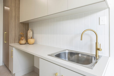 Modern laundry sink with brass tap, white tiled splashback, and minimalist cabinetry.
