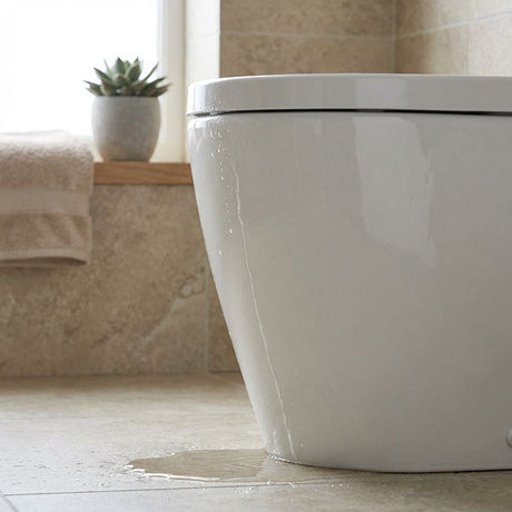 White toilet cistern leaking water onto beige tiled bathroom floor