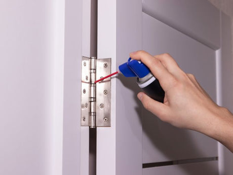 Hand spraying lubricant on metal door hinge for home maintenance and squeaky hinge repair