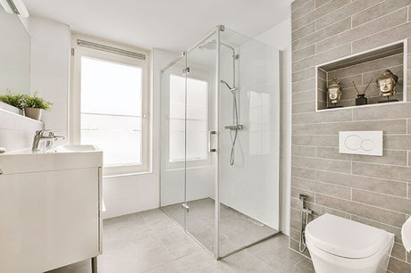 minimalist bathroom with glass shower enclosure, wall hung toilet, gray tile wall, and vanity sink