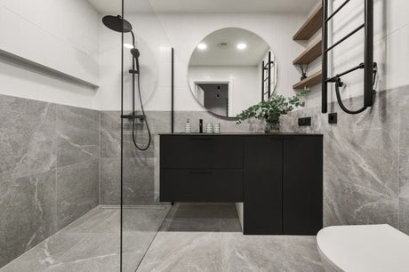 Modern minimalistic bathroom with grey stone tiles on walls and floor, black vanity furniture, and a round mirror