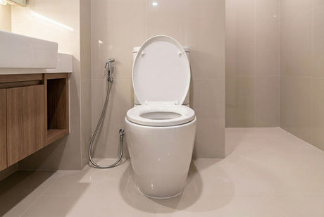 Modern bathroom with white toilet and bidet sprayer mounted on beige tiled walls