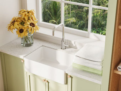 white apron-front laundry sink with chrome faucet on countertop beside folded towels and flowers