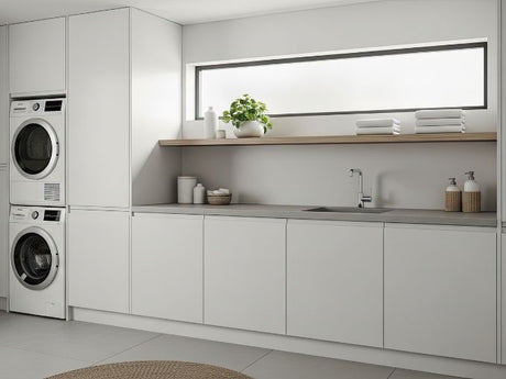 Modern laundry room with small laundry sink, long counter, white cabinets, and stacked washer dryer.