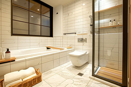 Modern marble tile bathroom with glass shower, bathtub, wall toilet, and towel basket.