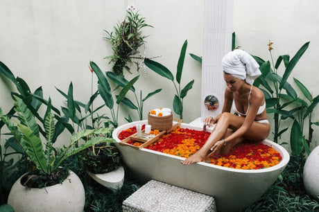 Woman in outdoor flower bath surrounded by tropical plants and white towels