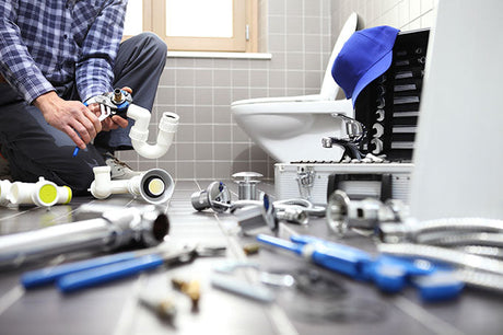 plumber assembling sink drain pipes with tools and plumbing parts on bathroom floor