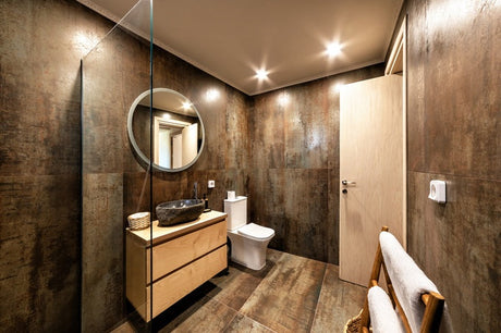 Industrial bathroom with wood vanity, stone vessel sink, round mirror, and rustic tile.
