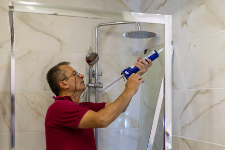 Applying silicone sealant to seal a glass shower screen during installation.