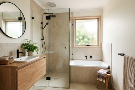 Neutral bathroom with glass shower, stone-tiled bath, timber vanity and round mirror