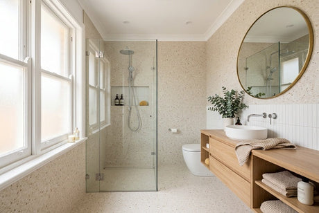 Narrow bathroom with terrazzo tiles, glass shower, timber vanity and round gold mirror