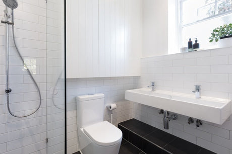 Compact white bathroom with subway tiles, glass shower, twin taps and black floor tiles