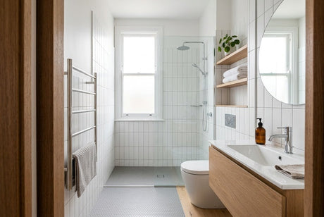 Narrow white-tiled bathroom with timber vanity, glass shower, and heated towel rail