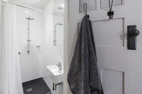 Compact white subway-tiled ensuite with rainfall shower, small basin and grey towel on door hook