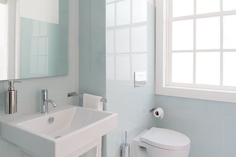 Small modern bathroom with wall-mounted sink, toilet, frosted window, and light blue tile walls.