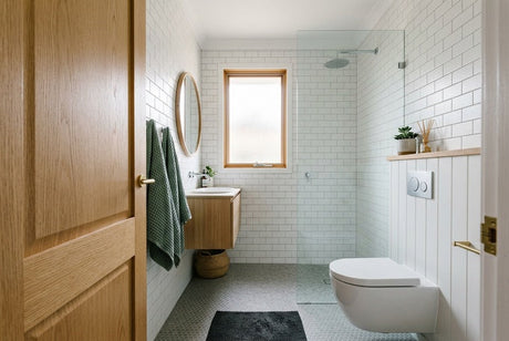 Small white subway-tiled bathroom with wall-hung toilet, timber vanity and round mirror