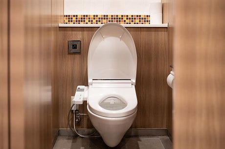 Smart toilet with bidet seat and control panel in compact wood-paneled restroom.