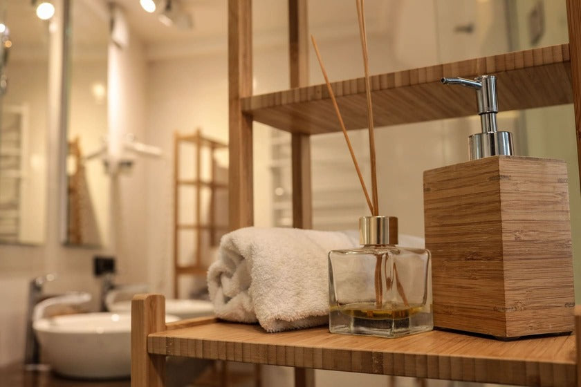 Warmly lit bathroom scene featuring folded white towels, fragrance diffusers and minimalist soap dispensers on a timber stair tiered display surface.