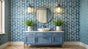 A stylish powder room featuring a round gold-framed mirror, blue vanity with white basin, and geometric patterned wallpaper