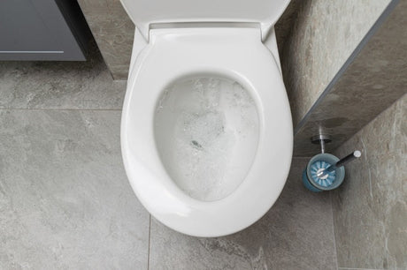 Toilet bowl flushing with water, viewed from above, with cleaning brush beside tiled floor.