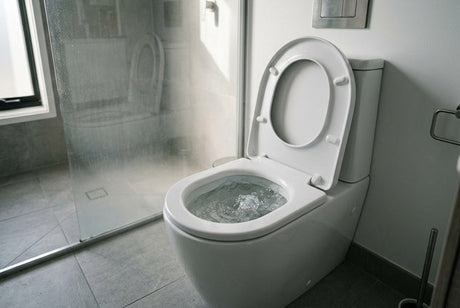 White wall-hung toilet flushing with swirling water, grey tiled bathroom